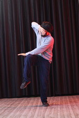 An Indian Dancer Boy Wearing over sized full sleeves T-Shirt and loose lower pants, dancing and posing in front of black curtain, 
