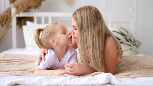 mom and daughter play, hug and kiss at home on the bed, lifestyle, tender relationship of a young mother and child, happy family and motherhood