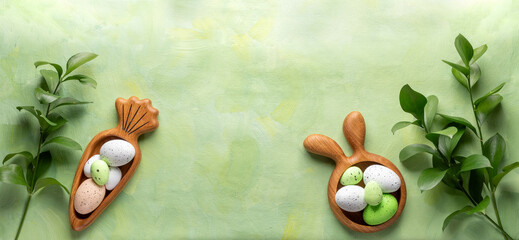 Wooden plates as bunny and carrot with Easter eggs, green Ruskus twigs on green yellow Copy space