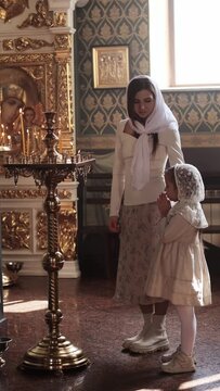 a mother and daughter in a temple or church are holding prayers or reciting a prayer, sad relatives, people are putting candles, introducing children to the sacraments of the church