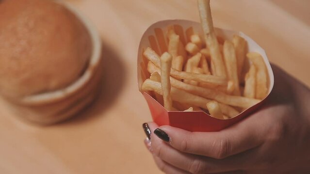 Closeup image of a woman holding and eating french fries and hamburger with fried chicken on the table at home