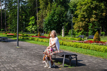 Woman and dog - Cavalier King Charles Spaniel - relaxing in a public park with lush flowers, plants, grass and trees