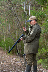 A hunter loads a shotgun at the edge of the forest