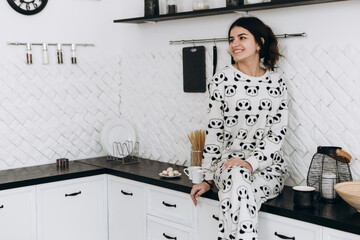 Cheerful woman standing in bright kitchen smiling laughing dressed in patterned pajama set. The...
