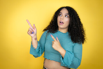 African american woman wearing casual sweater over yellow background surprised and pointing her...