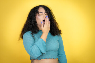 African american woman wearing casual sweater over yellow background bored yawning tired covering...