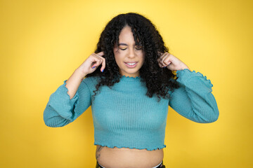 African american woman wearing casual sweater over yellow background covering ears with fingers...