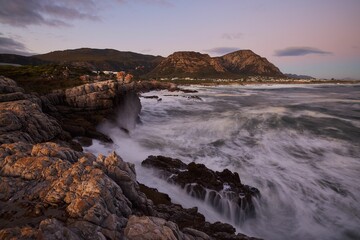 Fototapeta na wymiar Beautiful sunset over a rocky coast, with waves crashing against the shore. Hermanus, Western Cape.