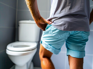 An image depicting a middle-aged man experiencing the discomfort of cystitis, symbolized by his grimace and the gesture of holding his crotch, indicative of painful or difficult urination - obrazy, fototapety, plakaty