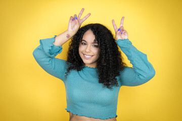 African american woman wearing casual sweater over yellow background Posing funny and crazy with...