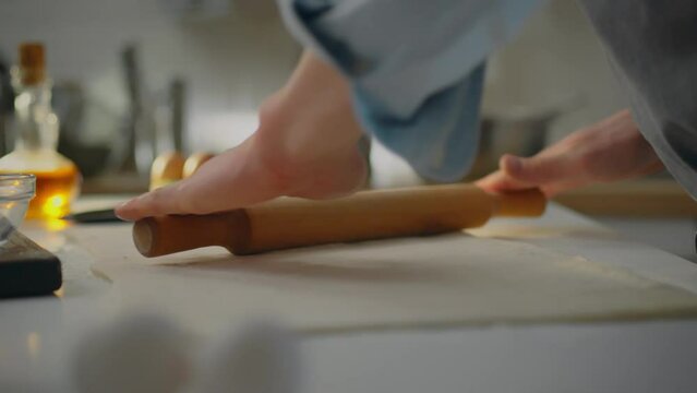 Kitchen. A professional baker dressed in an apron concentrates on preparing dough for baking in a bakery. Close-up of an experienced man working with puff pastry using trendy cooking recipes, handsome
