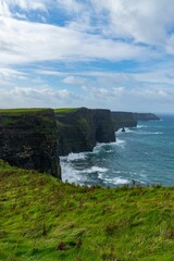 Lush, green grassy field with gentle waves lapping against the cliffs on a cloudy day