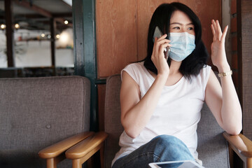 Asian businesswoman is wearing mask prevent for civid-19 and calling with smartphone in living...