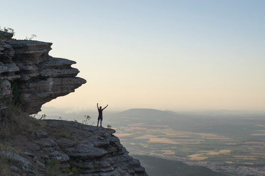 A Person Standing Atop A Majestic Mountain With Arms Raised, Overlooking The Beautiful View Below