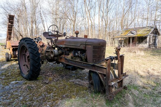 an old tractor parked in front of a shack in the woods