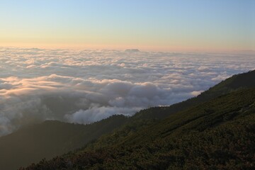 Scenic view of green mountains covered with clouds at sunset