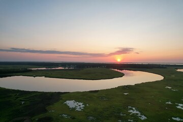 Aerial view of a river flowing through a green landscape at sunset
