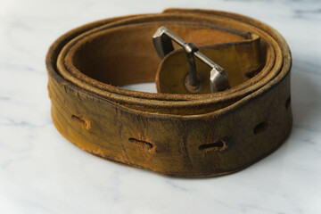 old and worn out brown leather belt on top of white table