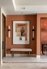 A modern and elegant entryway with terracotta walls, featuring an abstract art frame on the wall above a bench in neutral tones. The room has minimalist decor, a sleek desk against one of the walls.