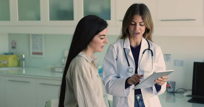 Latin GP showing to woman patient health test results using modern digital tablet device, explain treatment plan, prescribe medications during visit in private clinic. Healthcare, check-up, technology