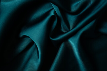 Emerald green silk or satin, draped fabric, elegant background. Beautiful wavy space for design Close-up images are blurry or blurred.