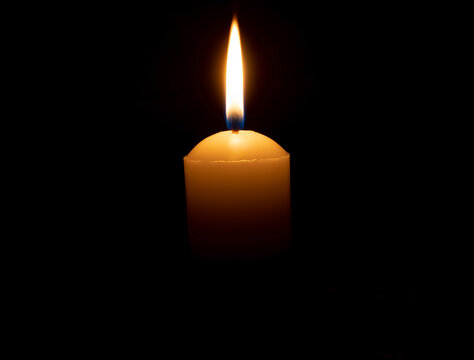 Single burning candle flame or light glowing on big white candle on black or dark background on table in church for Christmas, funeral or memorial service with copy space