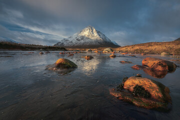 Calm river with stones on the foreground at the foot of Buachaille Etive Mor. At the entrance to the valley of Glencoe in the Scottish Highlands, Scotland