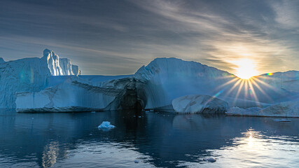 Blendenstern der Mitternachtssonne über Eisberg der in der Diskobucht bei Ilulissat in Grönland...