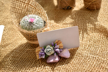 small blooming cactus in burlap covered pot and decorated table card on burlap background. Mockup