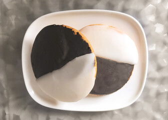 Two black and white cookies on a white plate photographed from above