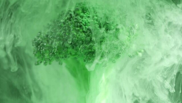 Fresh broccoli in cloud of green color paint in water. Artistic nutrition concept footage, 4K. Creative concept of vegetarianism, benefits of vegetables