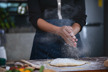 A woman stands in the kitchen and uses her hands to rub flour. which is the process of making pizza to food concepts and homemade pizza - obrazy, fototapety, plakaty