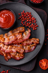 Delicious fresh fried bacon with salt and spices on a dark background