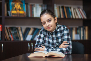 beautiful schoolgirl sitting in the library and reading a book