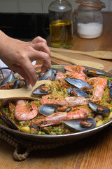 Cooking paella with shrimp and mussels using a wooden utensil in a home kitchen, typical Spanish cuisine, Majorca, Balearic Islands, Spain