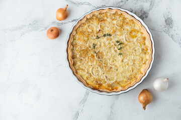 Flat lay of homemade onion cake on the white marble background. Quiche pie with steamed onions cheese and bacon