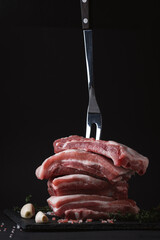 Close up shot of raw uncooked sliced pork meat surrounded by salt crystals, garlic and spices on the black background. Copy space for a free text. Cooking meat dishes recipe template.