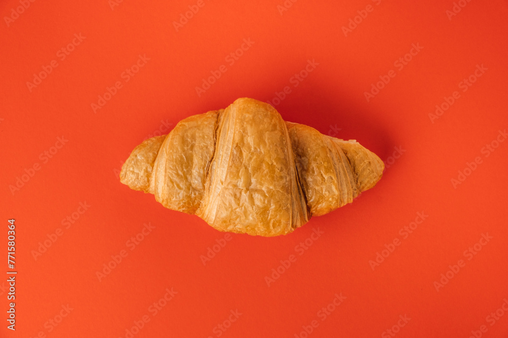 Wall mural Flat lay of single freshly baked croissant on the red background. Traditional French pastry with a copy space for a free text