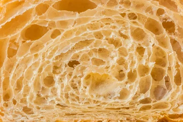 Schilderijen op glas Macro shot of fresh croissant cut in a half. Baked croissant dough textured background © alexanderon