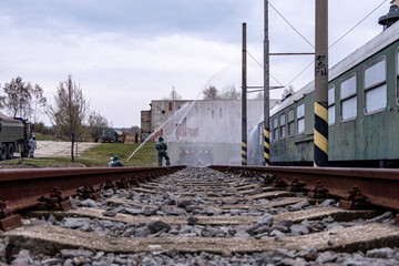 A train with a man in a green shirt spraying water on the tracks