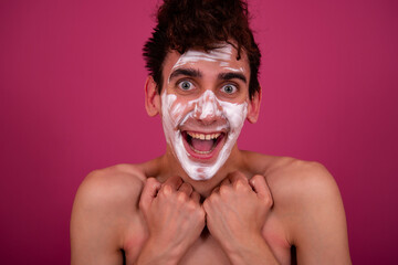 Funny guy takes a selfie with a cream mask. Facial care, anti-aging treatments. Pink background.