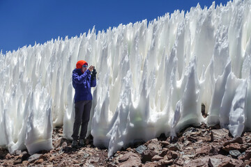 
A woman in the Atacama Desert, Chile, captures the towering penitentes with her camera. The ice formations, taller than herself, create a unique and surreal landscape.  - obrazy, fototapety, plakaty
