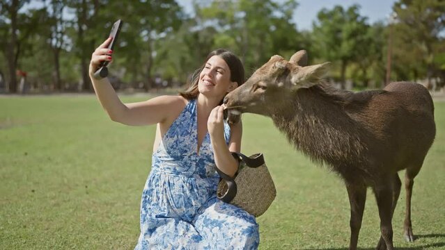 Cheerful, beautiful hispanic woman feeds deer crackers, snapping a selfie amid the wild nature of japan's nara park, radiating happiness in this unique travel adventure!