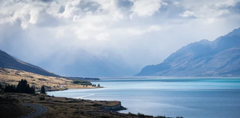 Crédence de cuisine en verre imprimé Aoraki/Mount Cook Alpine landscape scenery with azure lake, patches of sunlight and thick clouds of approaching storm