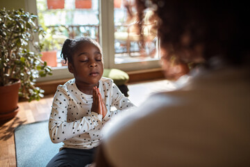 Young mother teaching her daughter how to do yoga and meditate at home