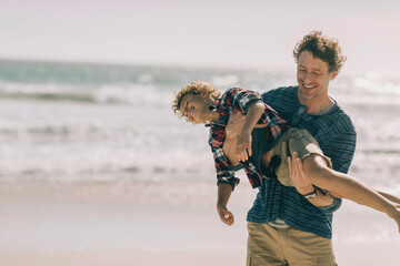 Smiling father and son having fun at the beach in casual clothes