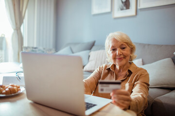 Smiling senior woman using credit card on laptop at home