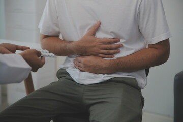 Man suffering with severe stomach pain sitting at home. Hand of mature guy holding abdomen...