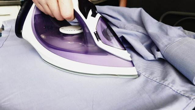 Top view person ironing blue t-shirt clothes at home. Doing household chores concept.