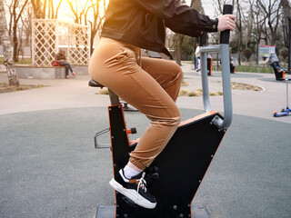 A girl in sportswear exercising on an exercise bike outdoors in a city park.